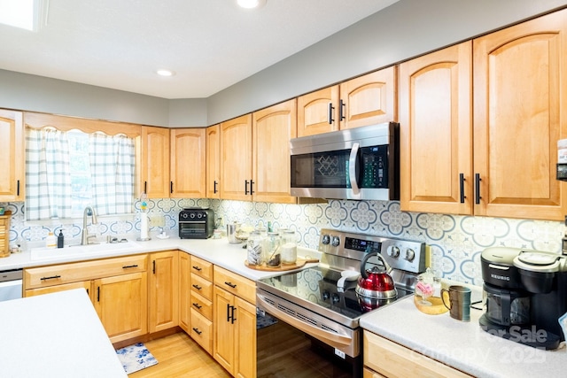 kitchen featuring stainless steel appliances, a sink, light countertops, light brown cabinetry, and light wood-style flooring
