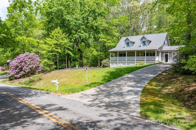 view of front of property featuring a front yard, covered porch, driveway, and a view of trees