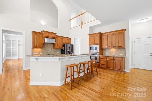 10024 Hazelview Dr, Charlotte, NC 28277 - kitchen featuring appliances with stainless steel finishes, under cabinet range hood, a breakfast bar area, light wood-type flooring, and brown cabinetry