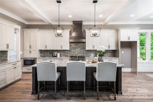 7703 Juniper Ln, Denver, NC 28037 - kitchen featuring custom exhaust hood, beam ceiling, a center island with sink, decorative backsplash, and stainless steel microwave