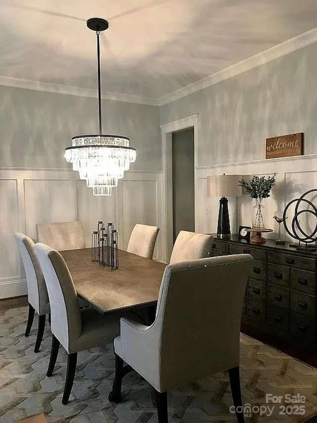 dining room with a decorative wall, a wainscoted wall, crown molding, and a chandelier