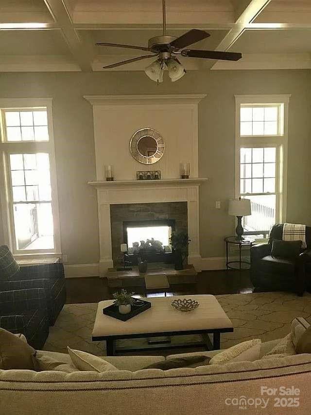 living area with coffered ceiling, a tiled fireplace, baseboards, a ceiling fan, and healthy amount of natural light