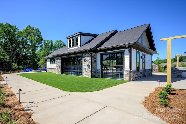 view of front of house with stone siding, a front lawn, roof with shingles, board and batten siding, and a garage