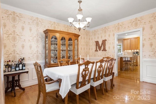 4389 Enchantment Cove Ln, Charlotte, NC 28216 - dining room featuring a chandelier, wallpapered walls, light wood-style floors, a wainscoted wall, and crown molding