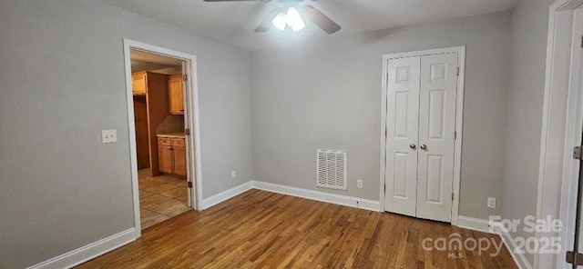 unfurnished bedroom featuring wood finished floors, a closet, baseboards, and ceiling fan