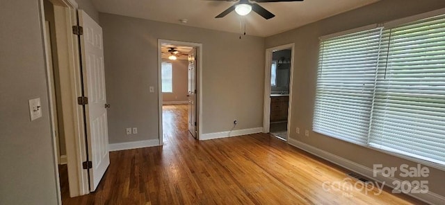 unfurnished bedroom featuring wood finished floors, baseboards, ensuite bath, and a ceiling fan