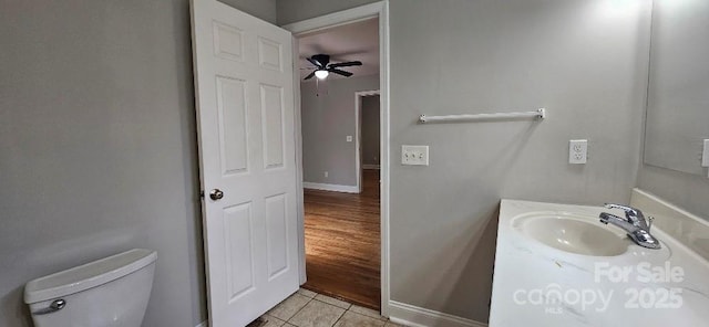half bath with tile patterned floors, toilet, baseboards, vanity, and ceiling fan