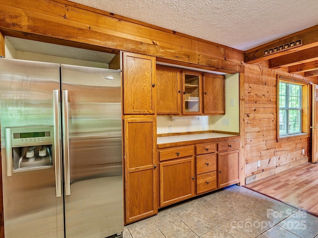 287 Sara Ridge Rd, Waynesville, NC 28786 - kitchen featuring stainless steel fridge with ice dispenser, brown cabinetry, light tile patterned floors, wood walls, and light countertops