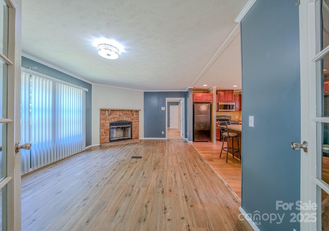 4065 NC-126 Hwy, Morganton, NC 28655 - unfurnished living room with light wood-style flooring, ornamental molding, a fireplace with raised hearth, a textured ceiling, and baseboards