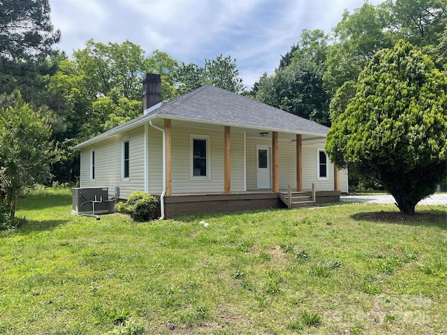 farmhouse-style home featuring covered porch, a chimney, a front lawn, central air condition unit, and a shingled roof