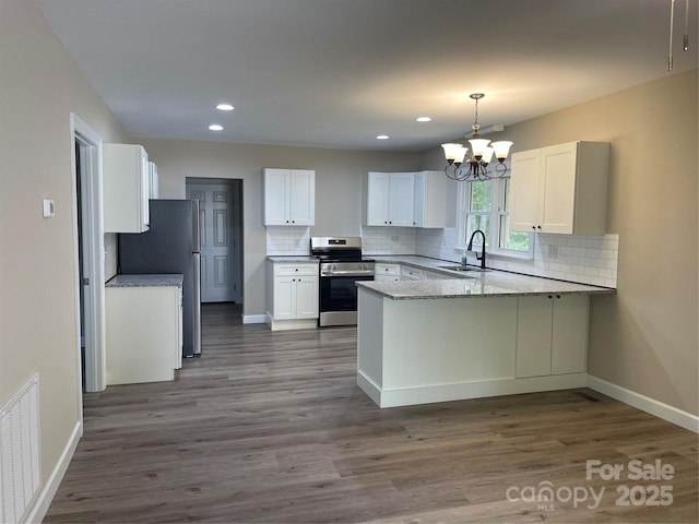 kitchen with stainless steel appliances, a sink, a peninsula, baseboards, and tasteful backsplash
