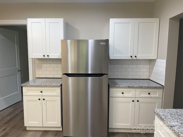 kitchen with freestanding refrigerator, tasteful backsplash, light stone counters, and white cabinetry