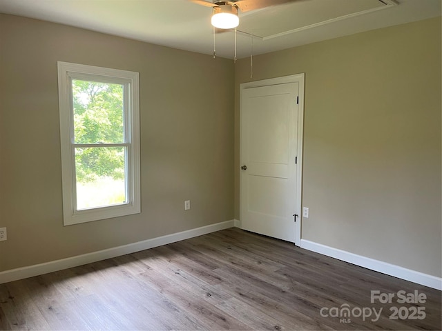 unfurnished room featuring attic access, wood finished floors, and baseboards