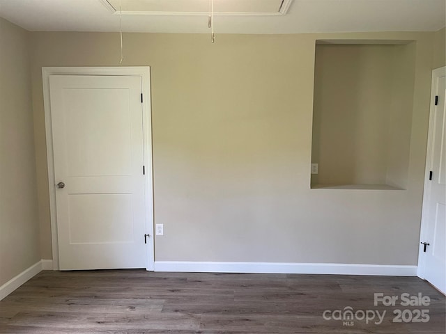 unfurnished room featuring attic access, wood finished floors, and baseboards