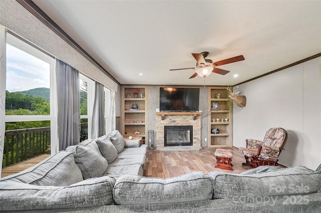 living room with wood finished floors, a ceiling fan, a fireplace, and built in features