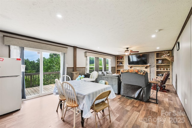dining room featuring a textured ceiling, wood finished floors, a ceiling fan, built in shelves, and a fireplace