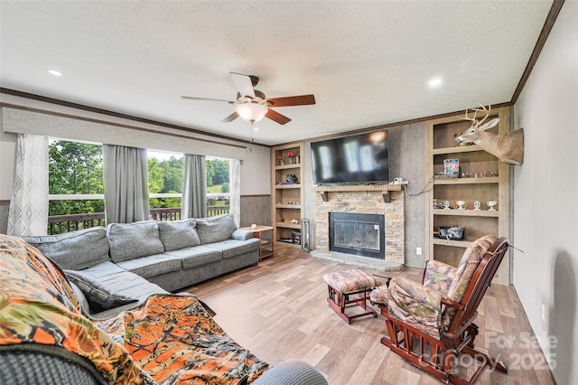 living area with ceiling fan, wood finished floors, crown molding, a stone fireplace, and a textured ceiling