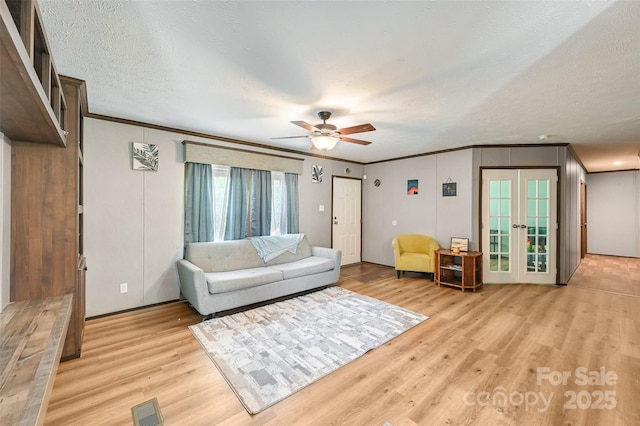 living room featuring ornamental molding, light wood-style floors, a ceiling fan, french doors, and a textured ceiling