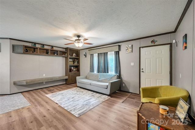 living room featuring ornamental molding, a ceiling fan, light wood finished floors, and a textured ceiling