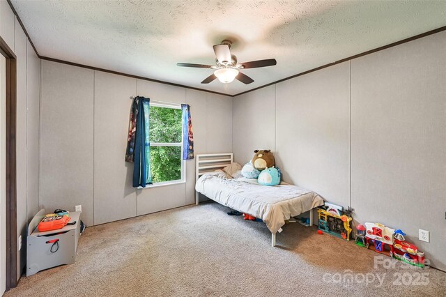 carpeted bedroom with a textured ceiling, ceiling fan, crown molding, and a decorative wall
