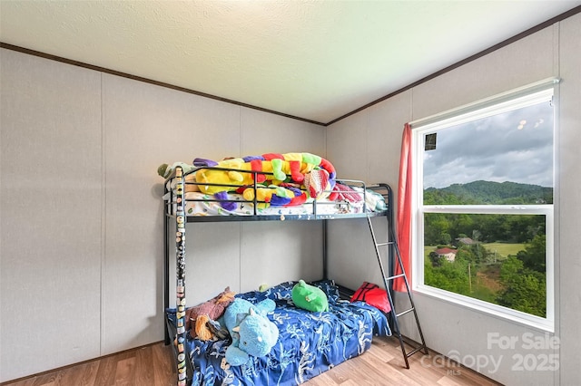 bedroom with a decorative wall, wood finished floors, and crown molding