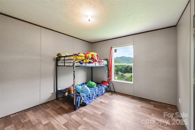 bedroom with wood finished floors, a textured ceiling, and crown molding
