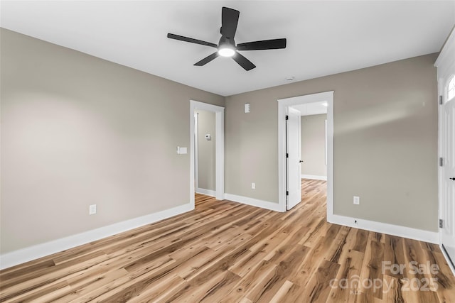 empty room featuring a ceiling fan, light wood finished floors, and baseboards