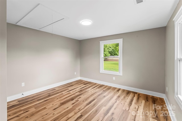 empty room with attic access, wood finished floors, and baseboards
