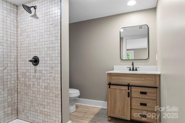 bathroom with tiled shower, toilet, vanity, baseboards, and recessed lighting