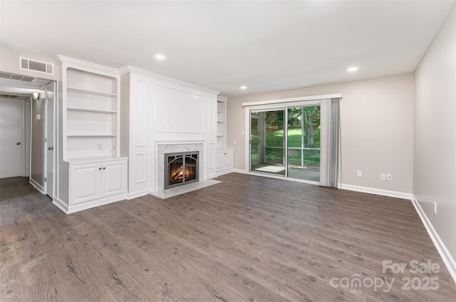 unfurnished living room featuring baseboards, dark wood-style flooring, a fireplace, recessed lighting, and built in shelves