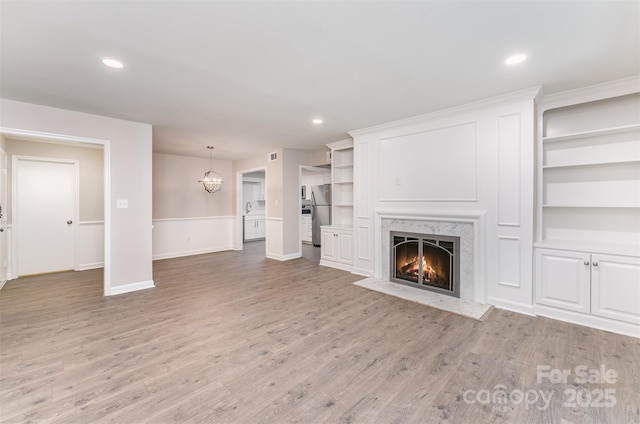 unfurnished living room with a premium fireplace, baseboards, light wood-style flooring, a chandelier, and recessed lighting