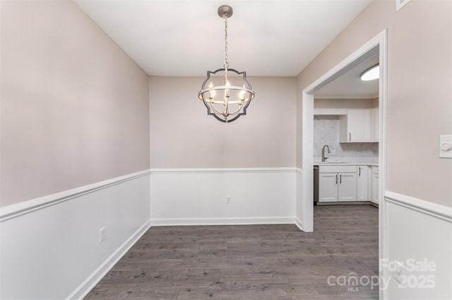 unfurnished dining area featuring a chandelier, dark wood finished floors, a sink, and baseboards