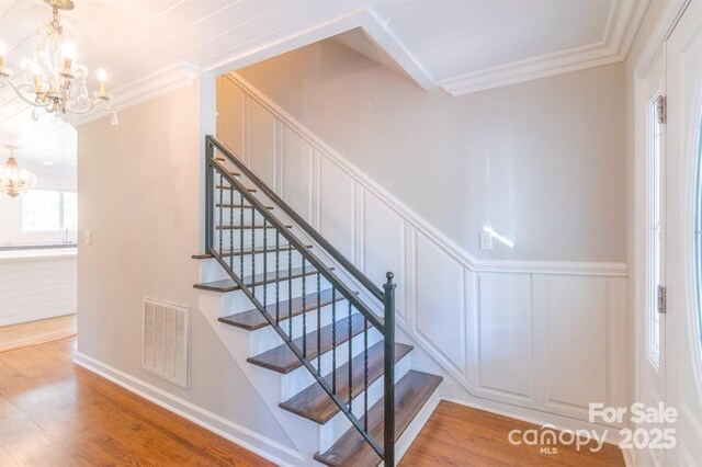 3921 Bon Rea Dr, Charlotte, NC 28226 - stairs featuring a chandelier, crown molding, wood finished floors, a decorative wall, and a wainscoted wall