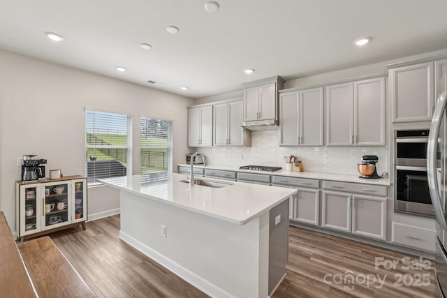 15023 Longmoore Dr, Charlotte, NC 28278 - kitchen with a sink, stainless steel gas stovetop, decorative backsplash, a center island with sink, and light countertops