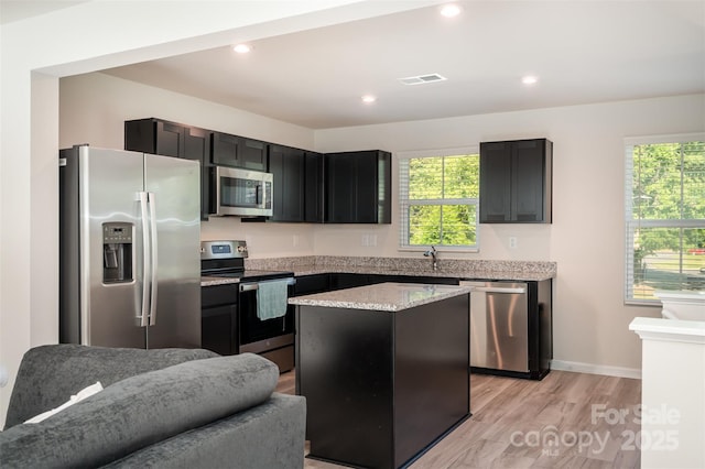 2037 Langer St, Charlotte, NC 28214 - kitchen featuring stainless steel appliances, light wood finished floors, a kitchen island, dark cabinets, and light stone countertops
