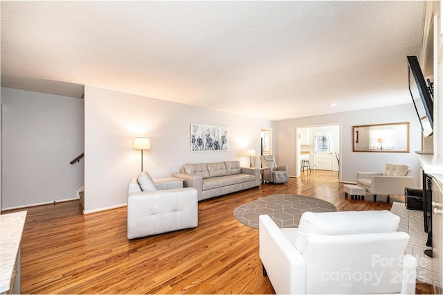 living area featuring light wood finished floors, stairs, baseboards, and a textured ceiling