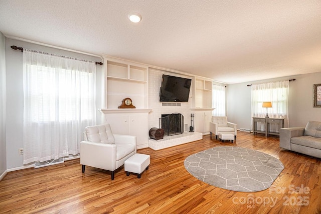 living room featuring wood finished floors, a fireplace, a textured ceiling, and baseboards