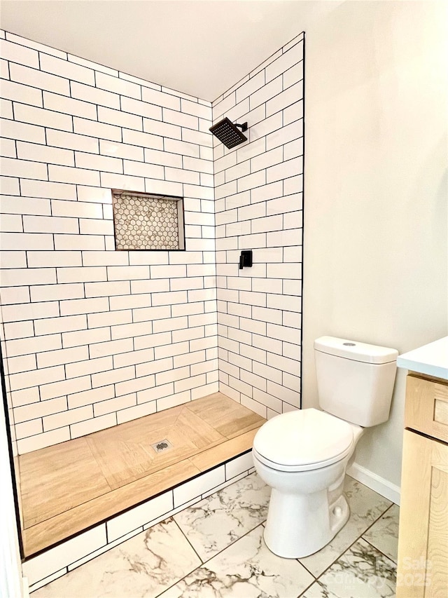 bathroom with marble finish flooring, toilet, vanity, a tile shower, and baseboards