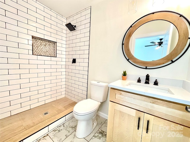 bathroom featuring marble look tile flooring, a tile shower, toilet, a ceiling fan, and vanity