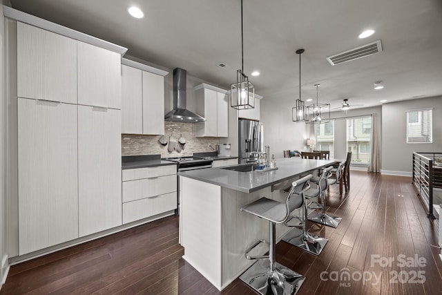 336 Uptown W Dr, Charlotte, NC 28208 - kitchen with wall chimney range hood, a breakfast bar area, an island with sink, tasteful backsplash, and dark wood-style floors