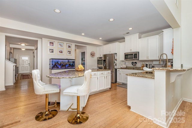 12822 Plumleaf Dr, Charlotte, NC 28213 - kitchen featuring stainless steel appliances, a breakfast bar area, light stone counters, light wood-style floors, and white cabinets