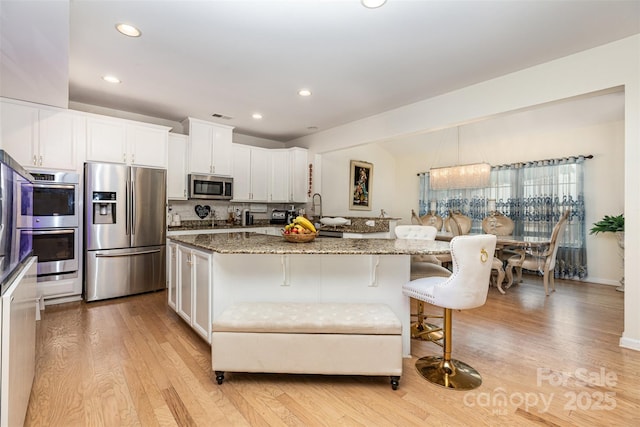12822 Plumleaf Dr, Charlotte, NC 28213 - kitchen featuring appliances with stainless steel finishes, a kitchen breakfast bar, light wood-style floors, light stone counters, and recessed lighting