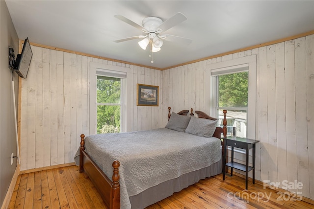 223 Smith Cove Rd, Candler, NC 28715 - bedroom featuring multiple windows, wood-type flooring, wooden walls, a ceiling fan, and baseboards
