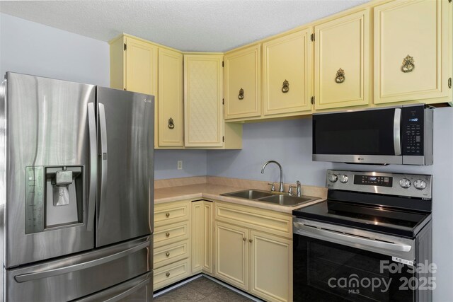 1075 Parkview Dr, Gastonia, NC 28054 - kitchen featuring appliances with stainless steel finishes, a sink, cream cabinetry, light countertops, and a textured ceiling