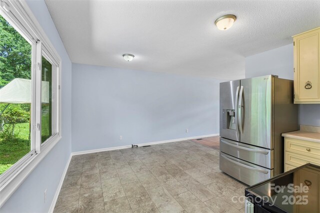 1075 Parkview Dr, Gastonia, NC 28054 - kitchen featuring stainless steel fridge, healthy amount of natural light, cream cabinetry, baseboards, and a textured ceiling