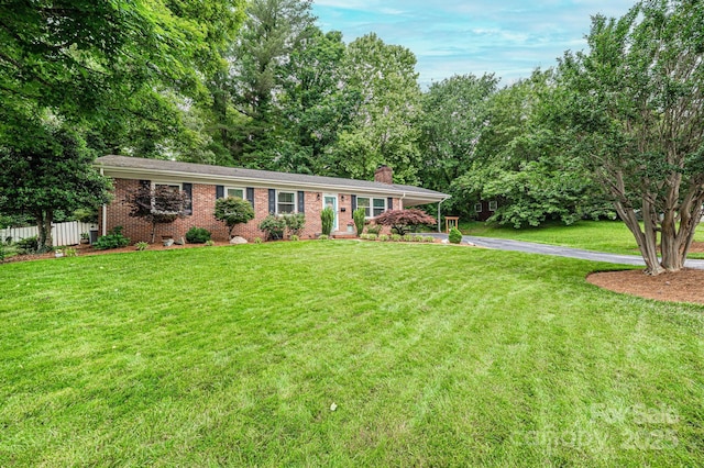 ranch-style home featuring a chimney, brick siding, and driveway