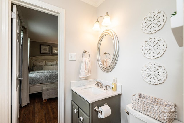 ensuite bathroom with ornamental molding, wood finished floors, toilet, and vanity