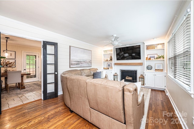 living area with a ceiling fan, wood finished floors, a fireplace, crown molding, and baseboards