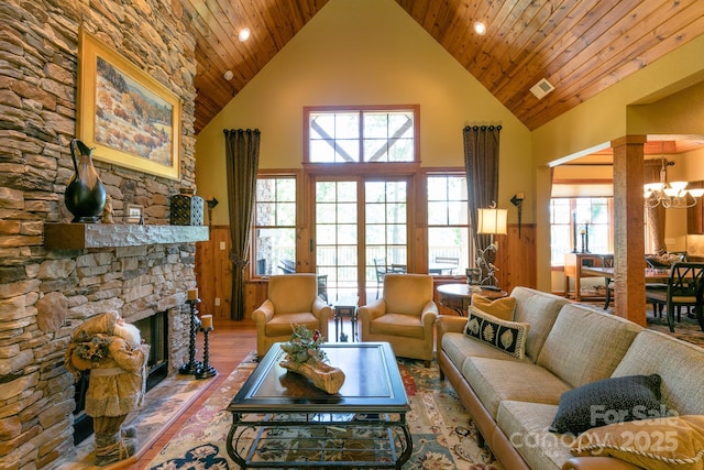 living area with high vaulted ceiling, wood finished floors, a stone fireplace, a chandelier, and wood ceiling
