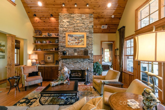 living room with hardwood / wood-style floors, high vaulted ceiling, wood ceiling, a stone fireplace, and wainscoting